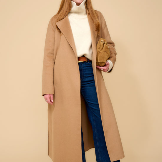 model shot wearing camel edge to edge wool coat, cream knit, blue jeans holding a camel handbag