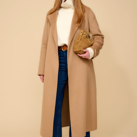 model shot wearing cream thick roll neck knit, denim jeans, camel coat and brown belt.