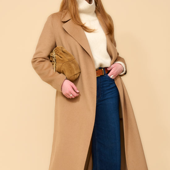 model shot wearing camel edge to edge wool coat, cream knit, blue jeans holding a camel handbag
