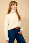 model shot wearing cream thick roll neck knit, denim jeans and brown belt.
