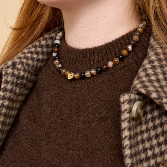 model close up shot wearing brown beaded necklace, brown knit and houndstooth coat.