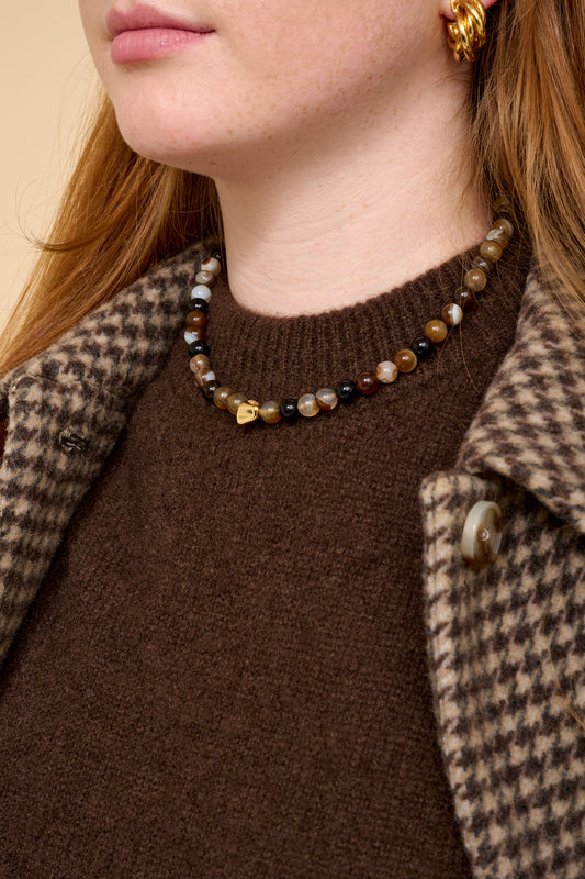 model close up shot wearing brown beaded necklace, brown knit and houndstooth coat.