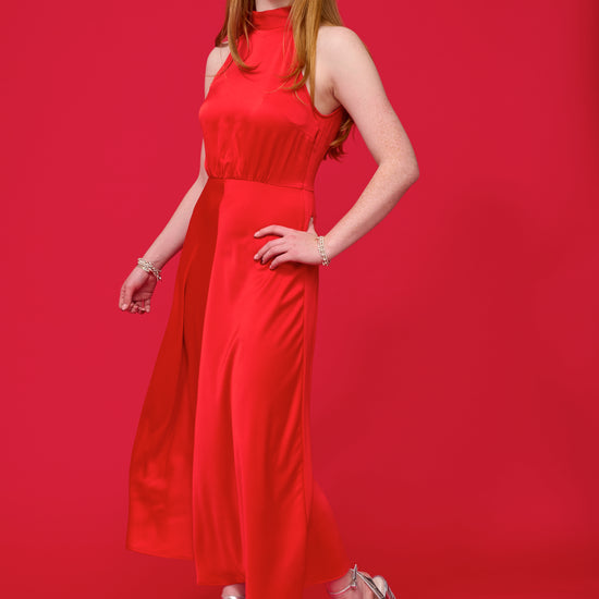 model shot wearing a red halterneck dress with open back and a tie and mid length from samsoe samsoe and silver heels with a red background