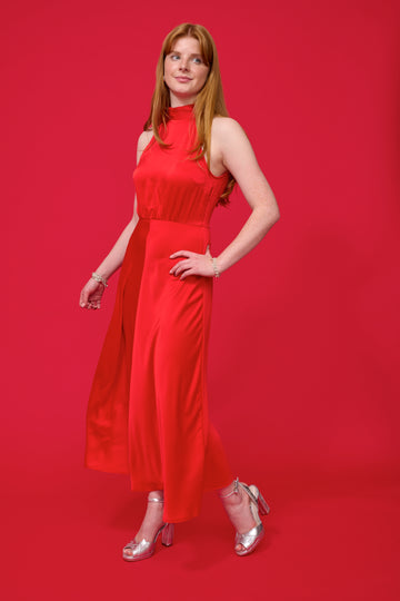 model shot wearing a red halterneck dress with open back and a tie and mid length from samsoe samsoe and silver heels with a red background