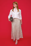 Model shot silver sparkly skirt worn with white crisp shirt and silver heels on a red background.
