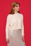 Woman wearing an ivory cashmere jumper and silver sequin skirt against a red background