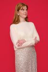 Woman wearing an ivory cashmere jumper and silver sequin skirt against a red background