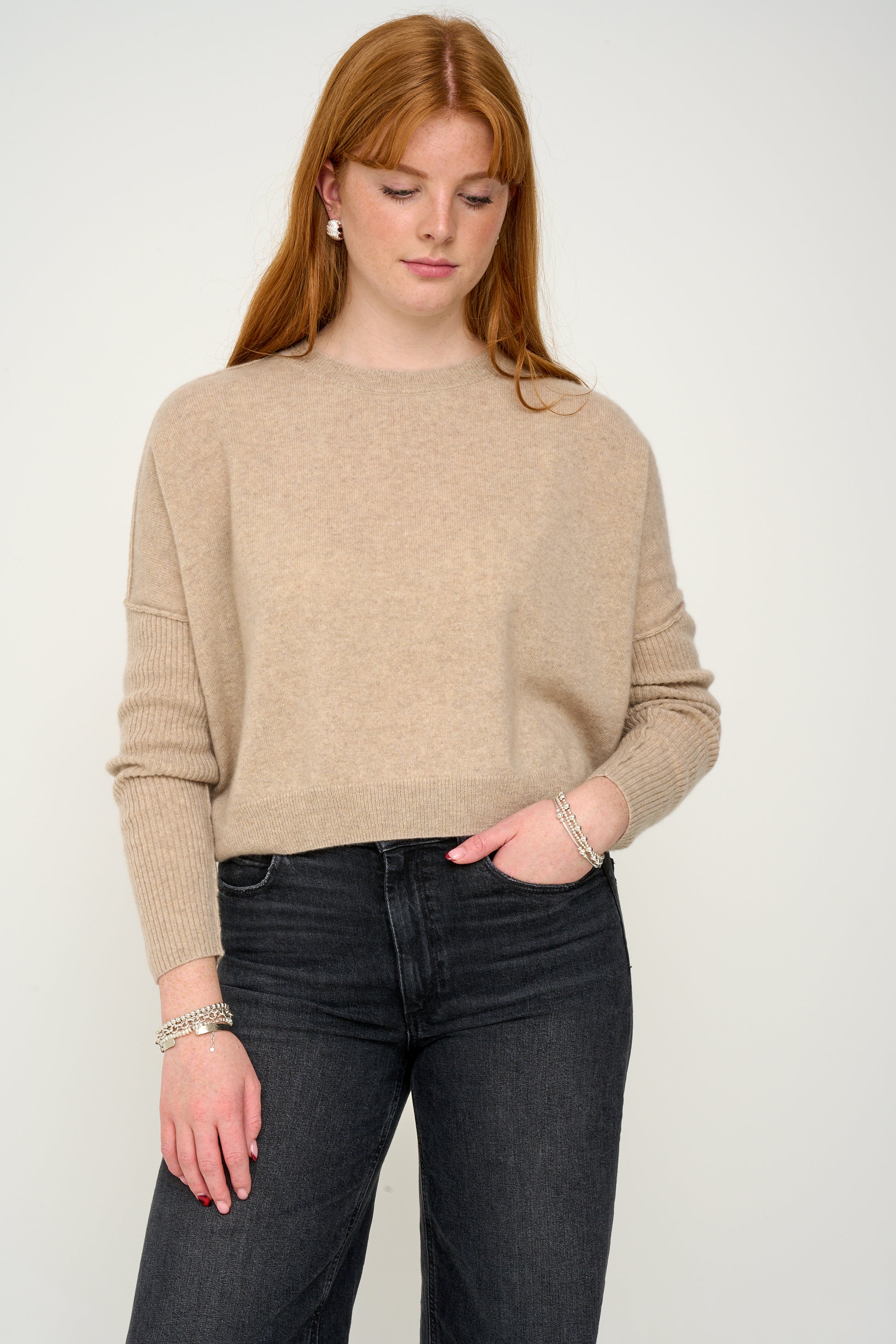 Woman wearing a oatmeal cashmere jumper with round neck and ribbed sleeves, black jeans against a plain background front view