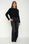 Woman wearing a black cashmere jumper with round neck and ribbed sleeves, dark jeans against a white background. Front shot.