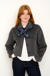 model shot wearing grey wool coat with navy polkadot silk scarf tied around shoulders.