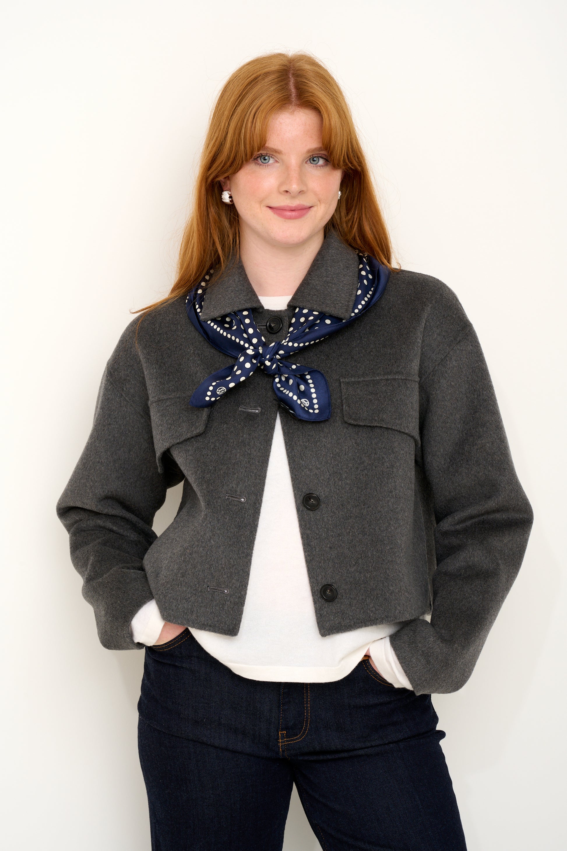 model shot wearing grey wool coat with navy polkadot silk scarf tied around shoulders.