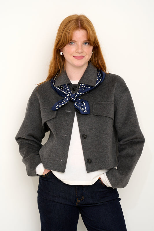 model shot wearing grey wool coat with navy polkadot silk scarf tied around shoulders.