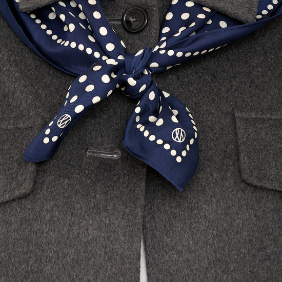 navy polka dot silk scarf tied around models shoulders layered with a grey wool jacket.