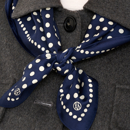 Close up shot of grey wool jacket detailing and silk navy polkadot scarf layered over shoulders.