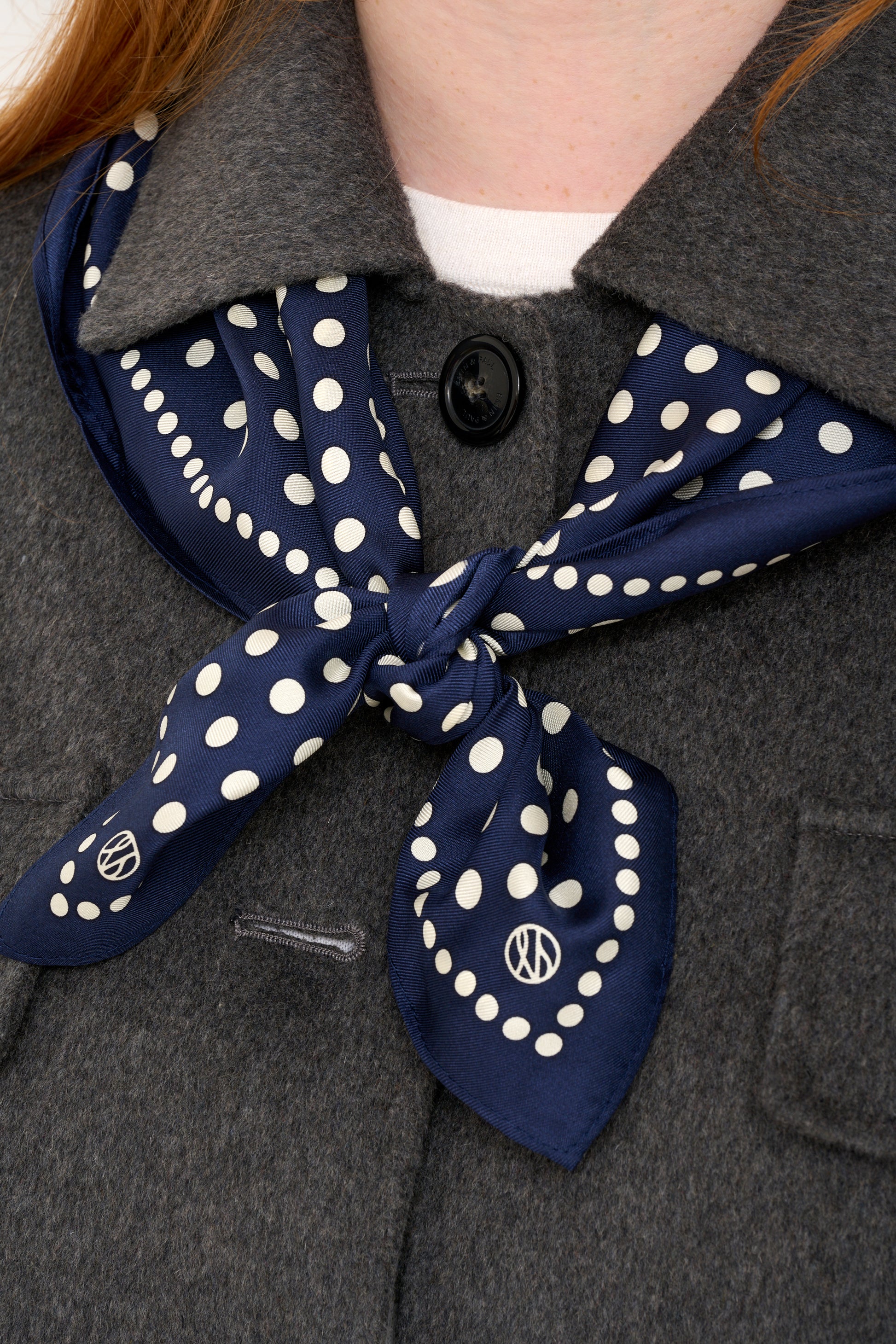 Close up shot of grey wool jacket detailing and silk navy polkadot scarf layered over shoulders.