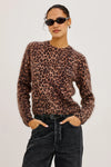 Person wearing a leopard print sweater and black pants on a plain background