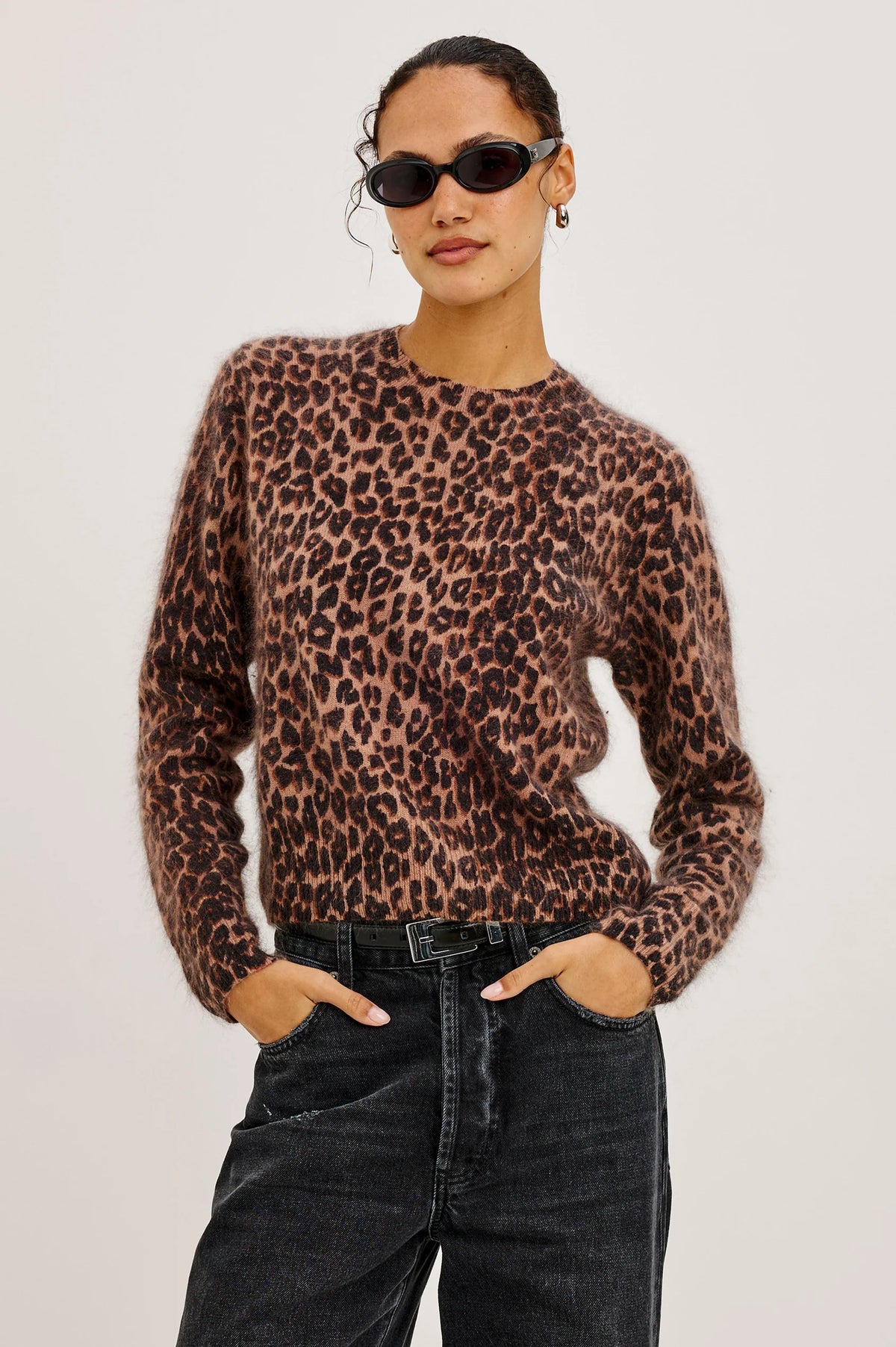Person wearing a leopard print sweater and black pants on a plain background
