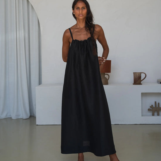 Woman wearing a black slip dress standing in a minimalistic room.