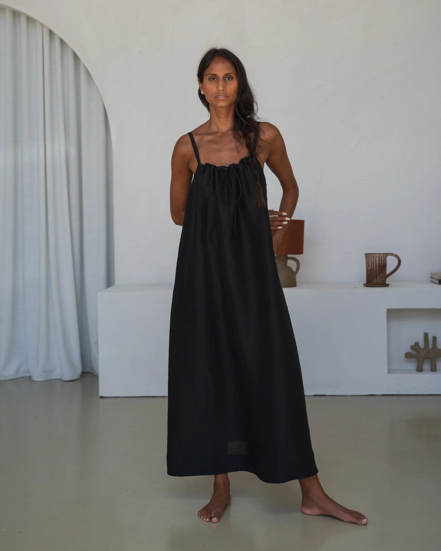 Woman wearing a black slip dress standing in a minimalistic room.