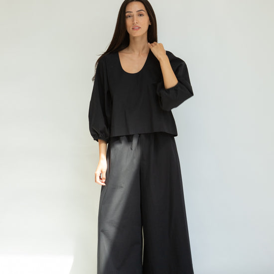 Woman wearing a black outfit with wide-leg pants against a white background