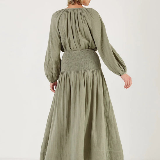 Woman wearing a green outfit, including a skirt by Mondo Corsini, on a white background. Rear View