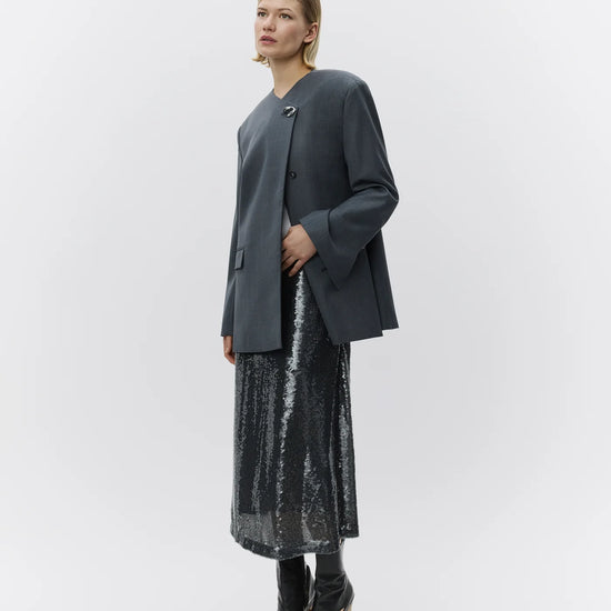 Woman wearing a dark gray blazer and black sequin skirt on a white background