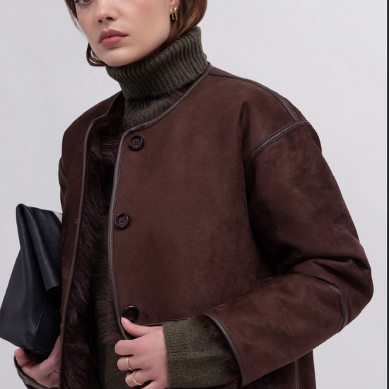 Woman wearing a brown coat over a green turtleneck on a white background