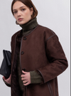 Woman wearing a brown coat over a green turtleneck on a white background
