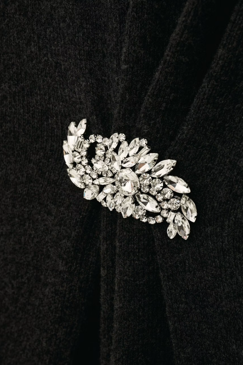 charcoal grey knitted long dress with round neck, ruche detailing with a statement crystal brooch and balloon sleeves close up