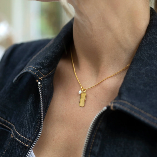 rectangular gold pendant with heart on one side and glimmer written on the other with pearl from claudia bradby model shot