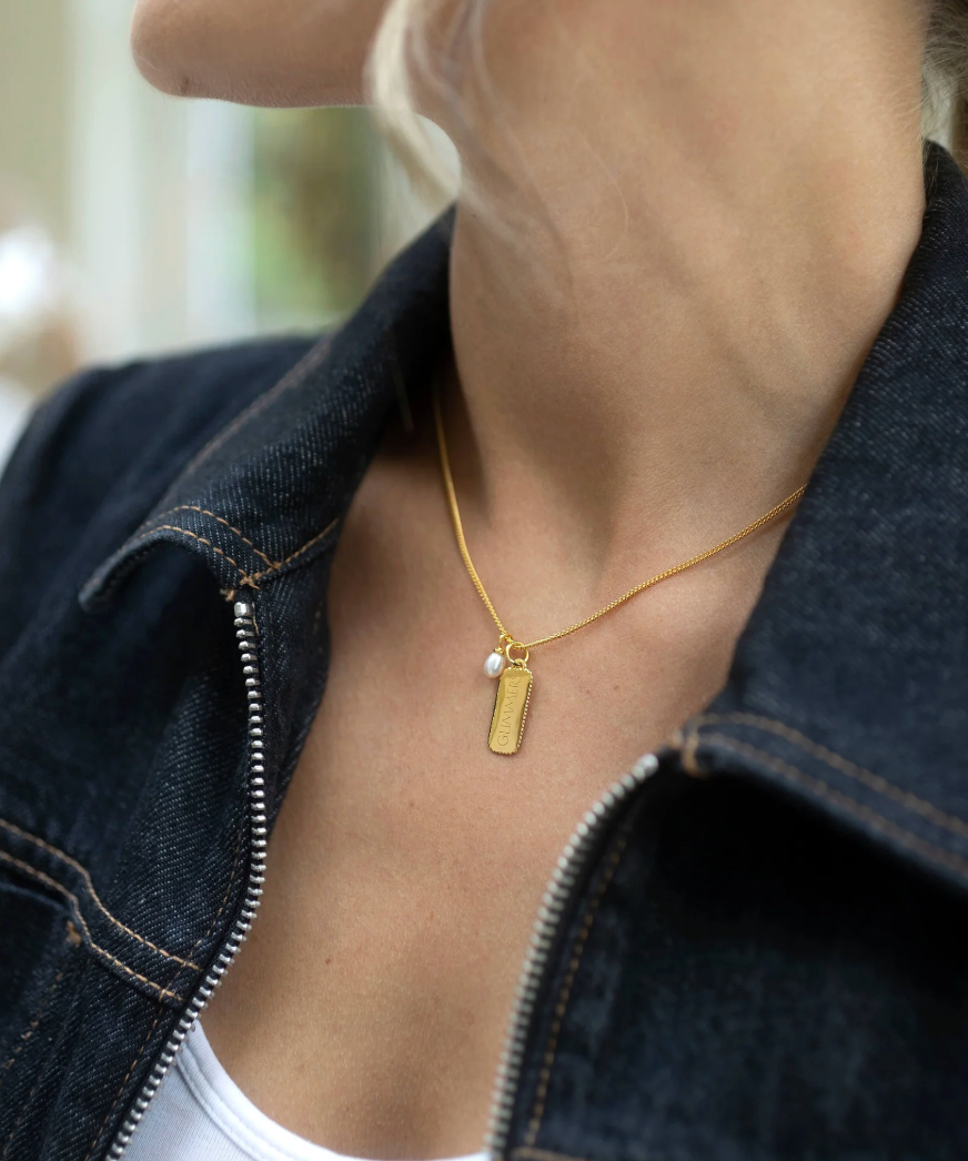 rectangular gold pendant with heart on one side and glimmer written on the other with pearl from claudia bradby model shot