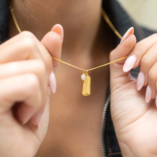 rectangular gold pendant with heart on one side and glimmer written on the other with pearl from claudia bradby model shot