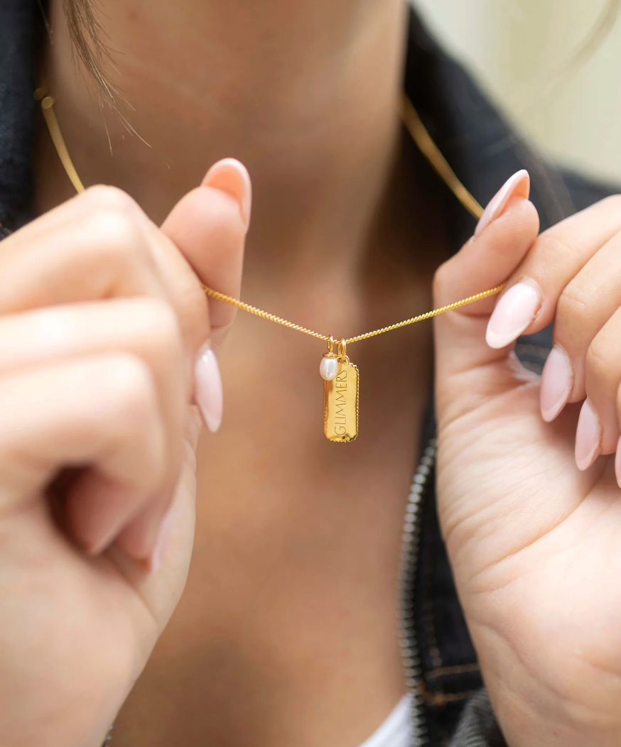 rectangular gold pendant with heart on one side and glimmer written on the other with pearl from claudia bradby model shot