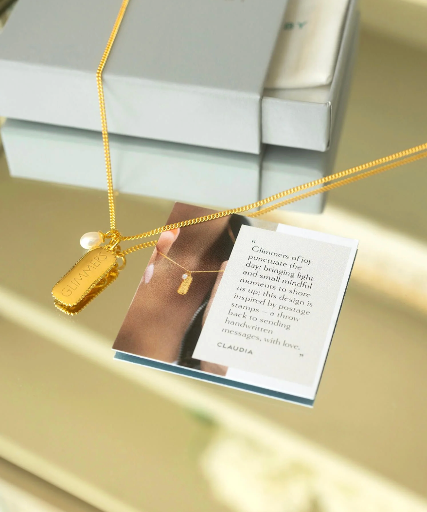 rectangular gold pendant with heart on one side and glimmer written on the other with pearl from claudia bradby 