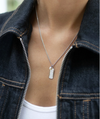 silver rectangular pendant necklace with heart on one side and glimmers on the reverse form claudia bradby model shot