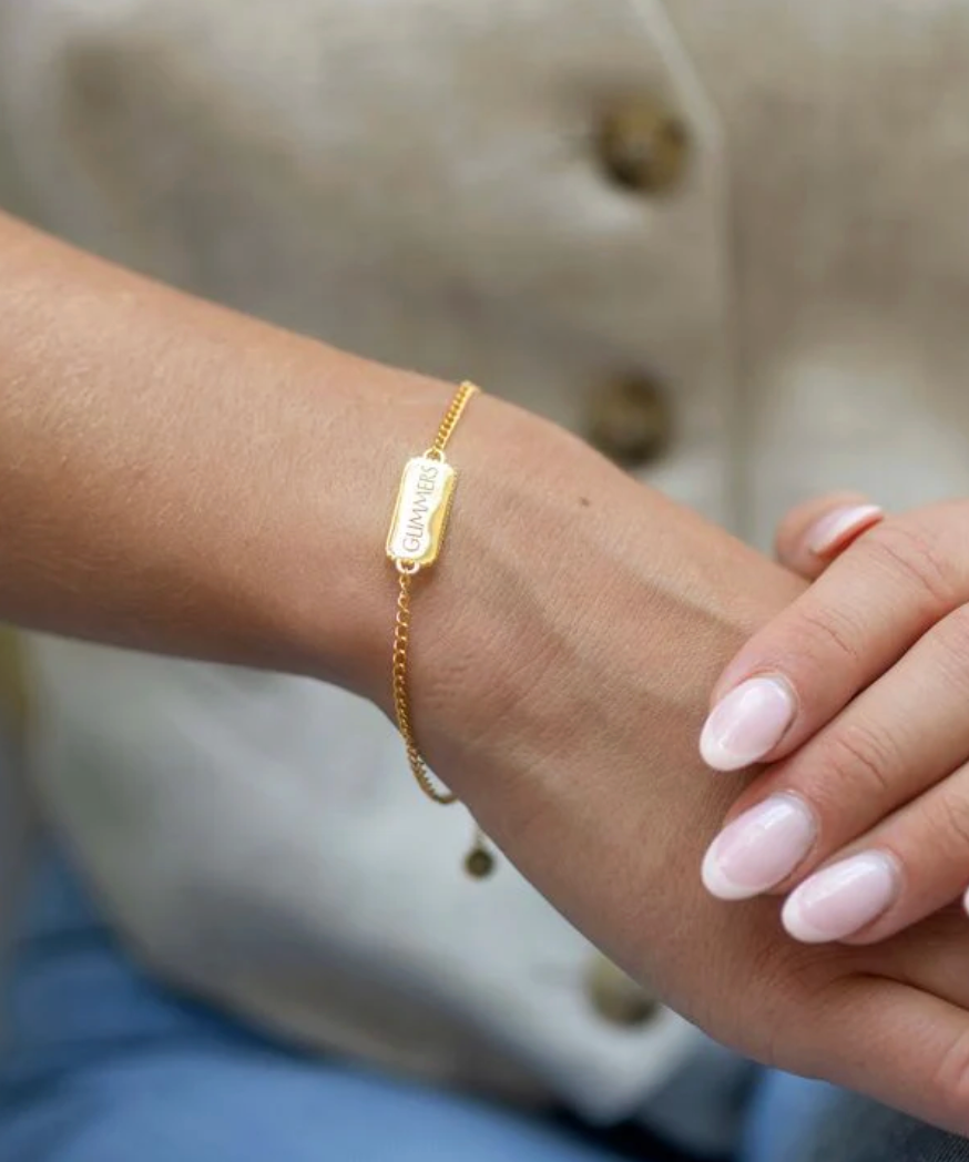 rectangular pendant bracelet with heart on one side and glimmers written on the other with a gold chain, lobster clasp and pearl form claudia bradby model shot