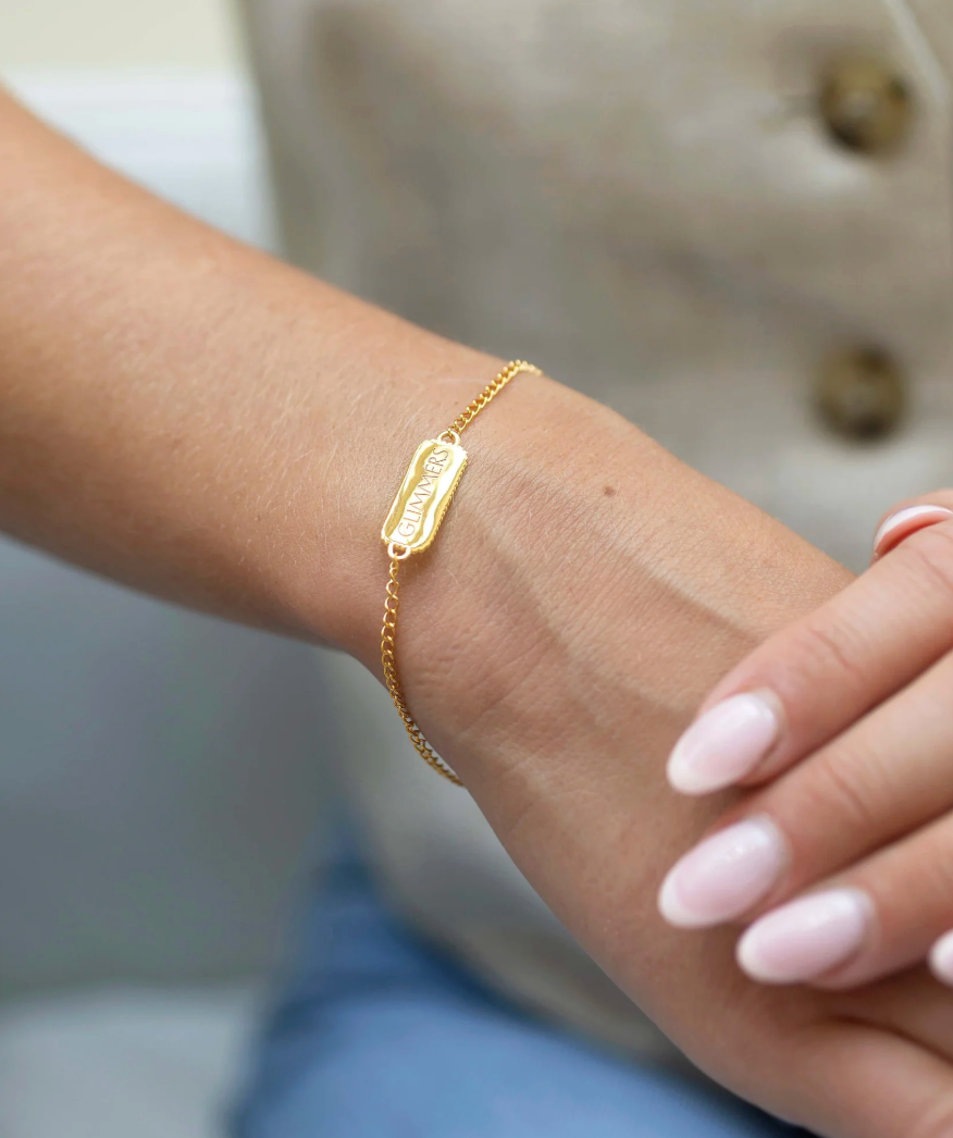 rectangular pendant bracelet with heart on one side and glimmers written on the other with a gold chain, lobster clasp and pearl form claudia bradby model shot