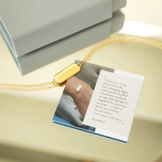 rectangular pendant bracelet with heart on one side and glimmers written on the other with a gold chain, lobster clasp and pearl form claudia bradby 