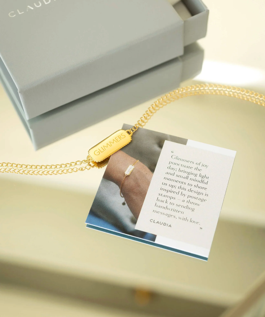 rectangular pendant bracelet with heart on one side and glimmers written on the other with a gold chain, lobster clasp and pearl form claudia bradby 