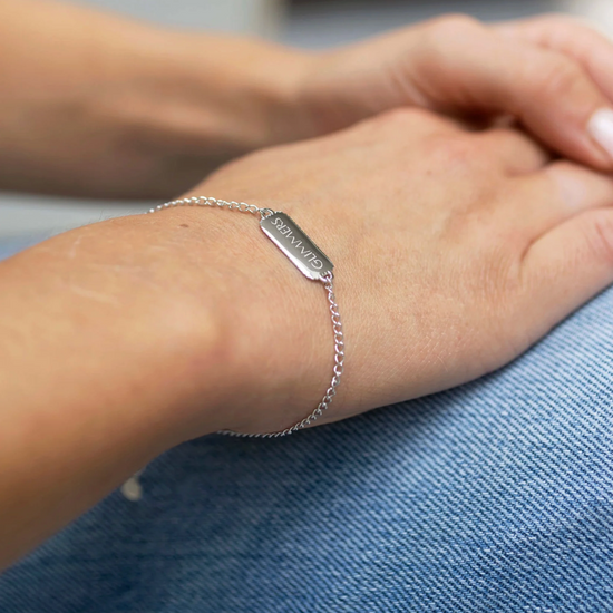 silver bracelet with rectangular pendant with a heart on one side and glimmers written on the other from claudia bradby model shot