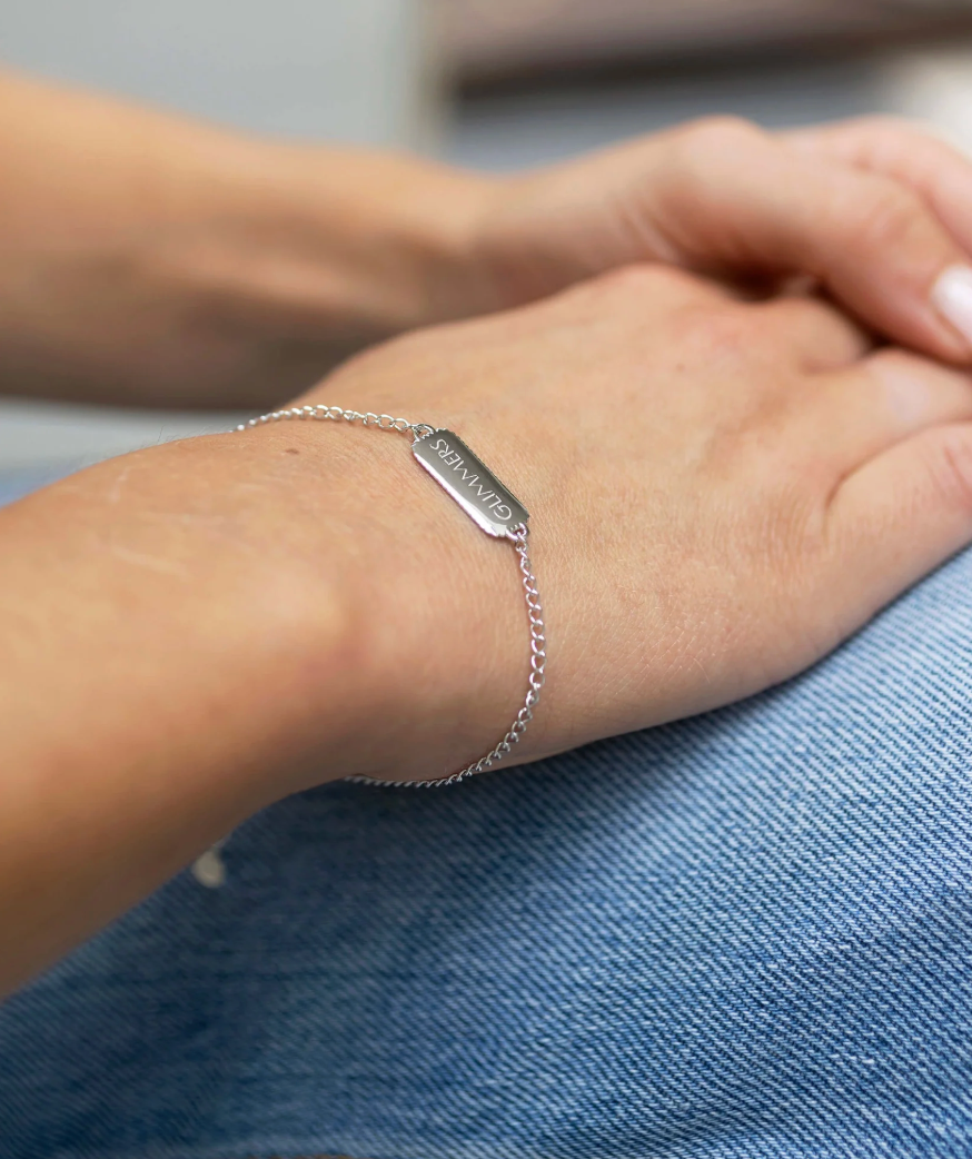 silver bracelet with rectangular pendant with a heart on one side and glimmers written on the other from claudia bradby model shot