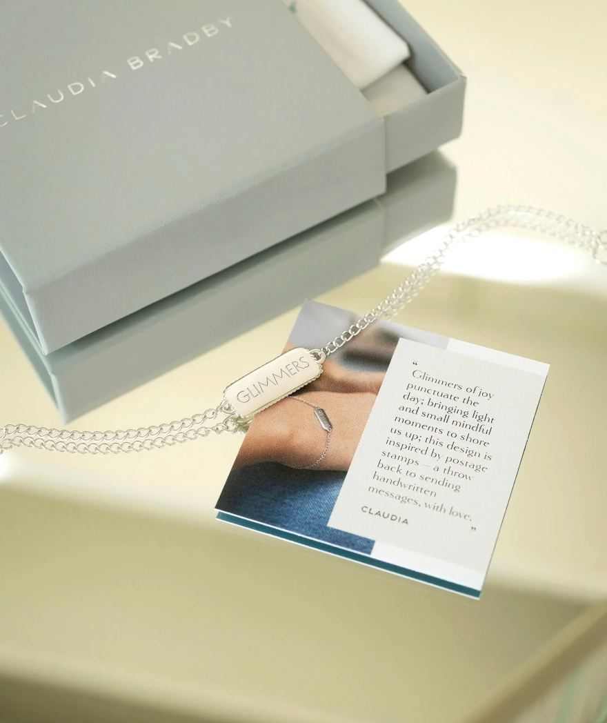 silver bracelet with rectangular pendant with a heart on one side and glimmers written on the other from claudia bradby 