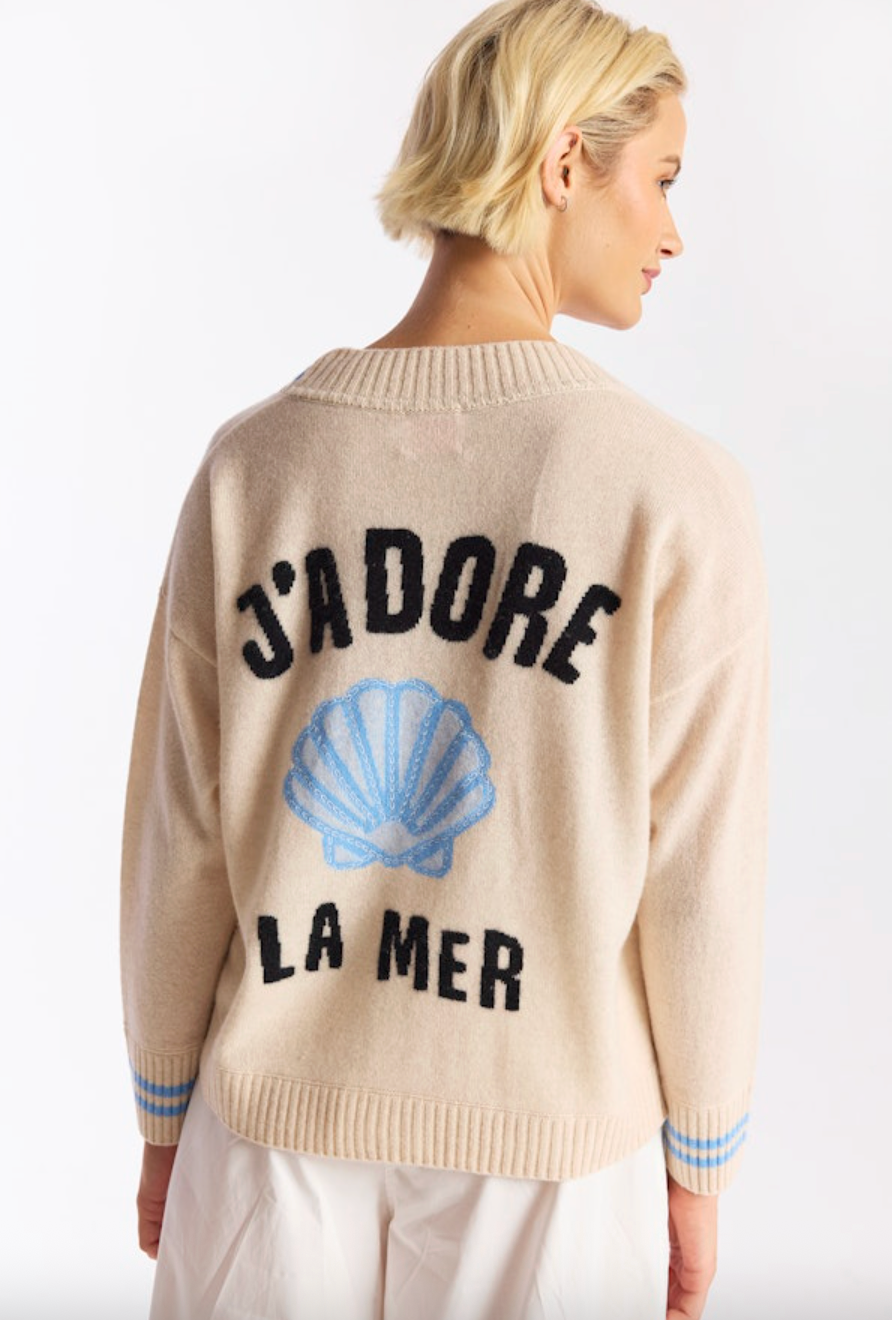 Person wearing a beige sweater with text and a shell design on a white background