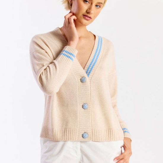 Woman wearing a beige cardigan with blue trim and buttons on a white background