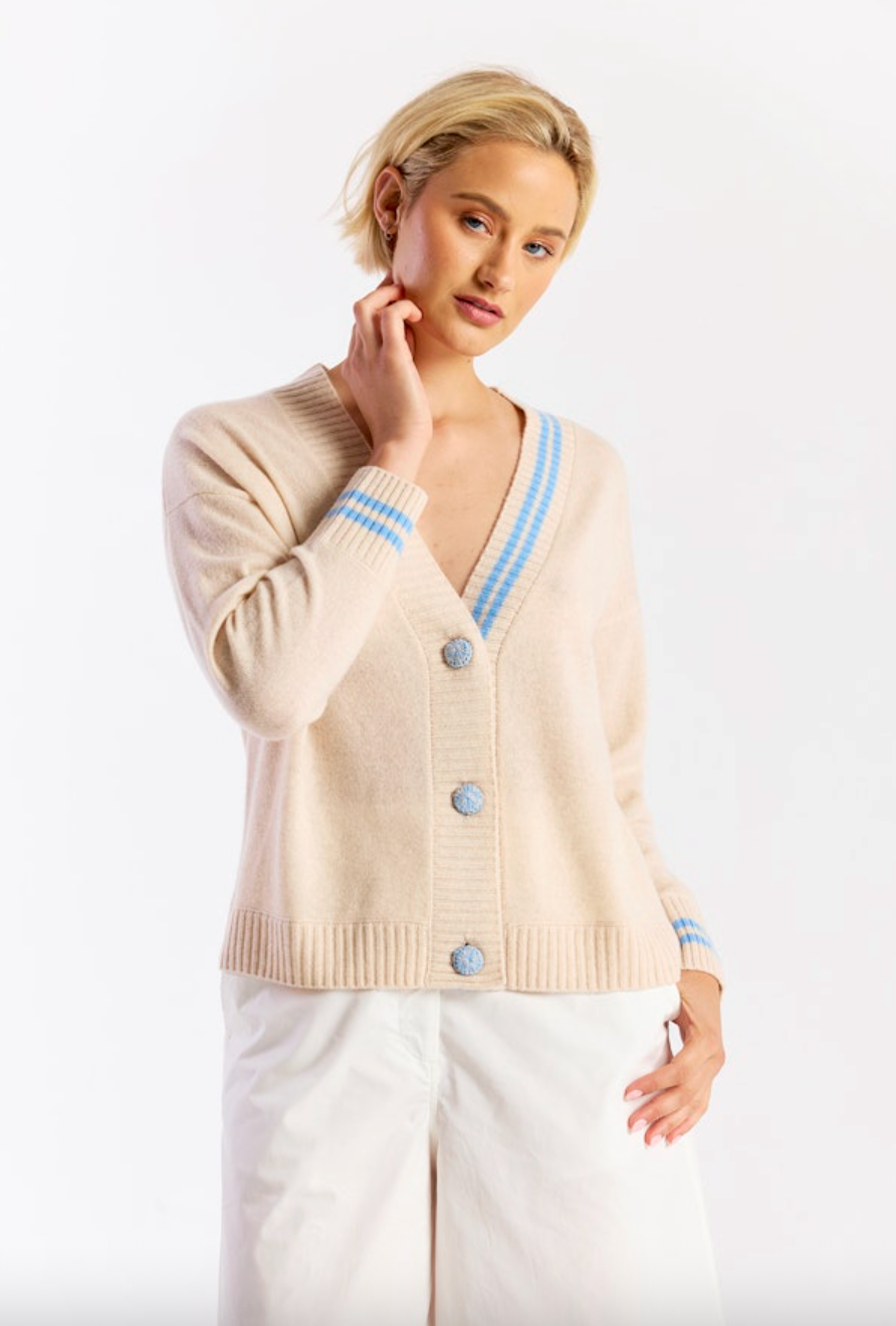 Woman wearing a beige cardigan with blue trim and buttons on a white background