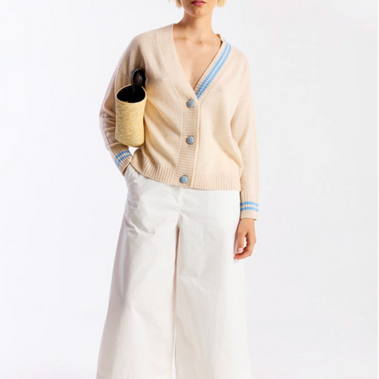 Woman wearing a beige cardigan, white pants, and sunglasses on a white background