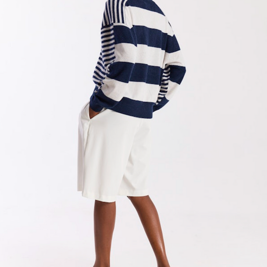 Person wearing a navy and white striped sweater with a white skirt on a white background