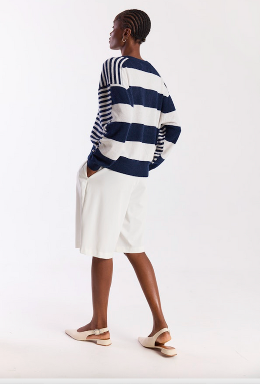 Person wearing a navy and white striped sweater with a white skirt on a white background
