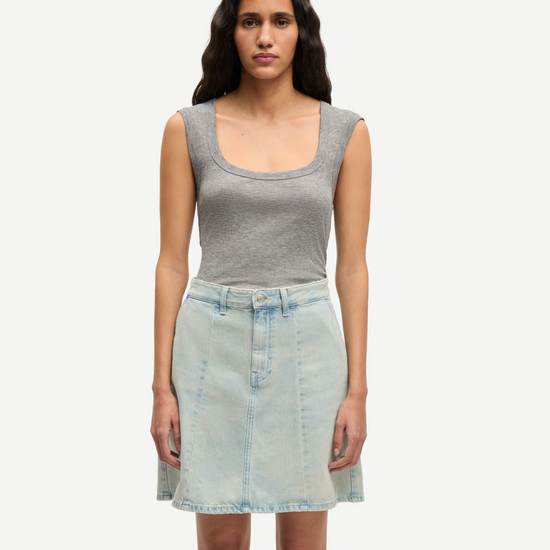 Woman wearing a gray tank top and light blue denim skirt on a white background