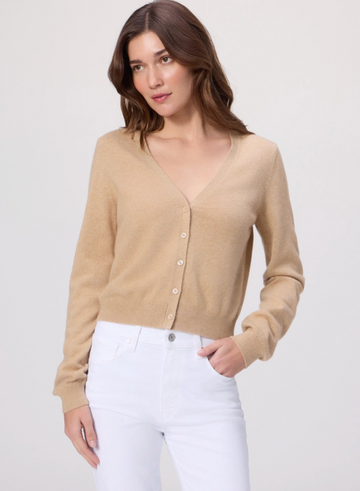 Woman wearing a beige cardigan and white pants on a light gray background